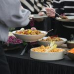 A diverse array of colorful dishes on a buffet table at a gathering, featuring salads and grains.